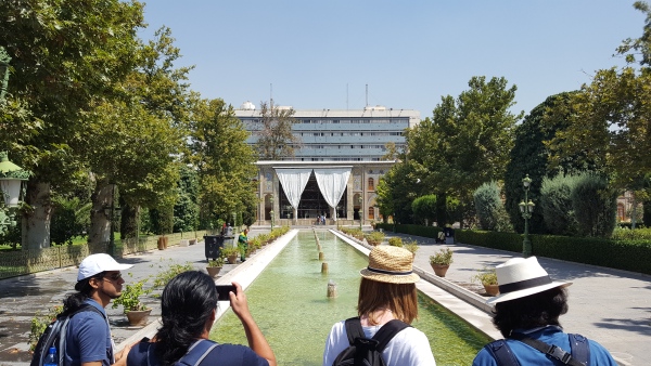 Et langt grønt basseng med fontener, og et stort bygg i bakgrunnen